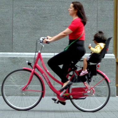 Frau auf Fahrrad mit Kind auf Kindersitz