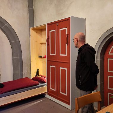 Schrankbett auf der Pilgerwanderung. Im Vordergrund betrachtet ein Mann das Schrankbett